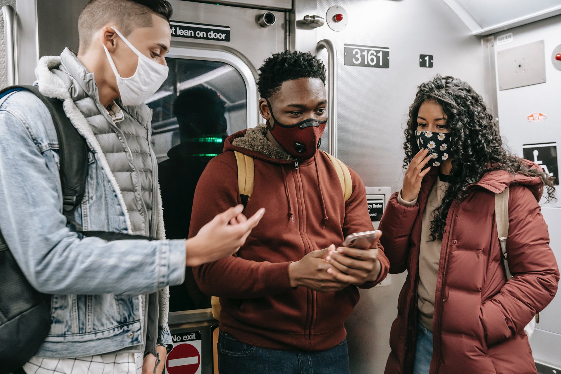 faceless multiethnic students in masks in subway train with phone